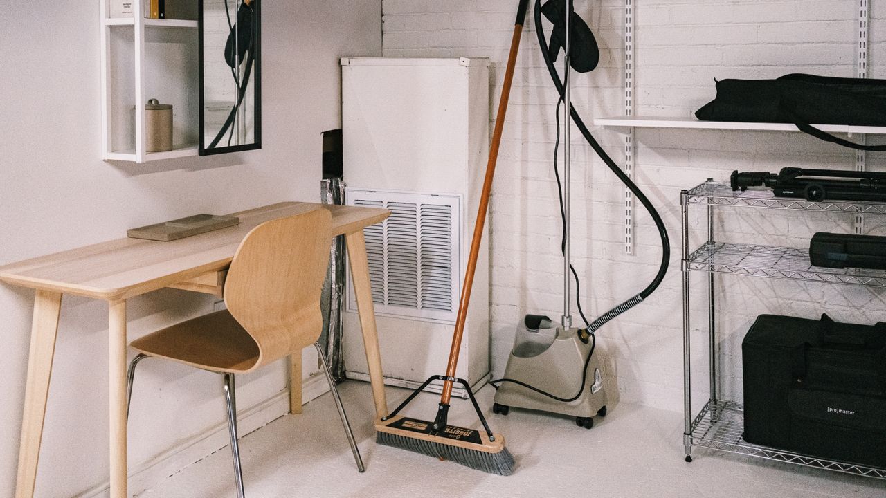 Un bureau à domicile bien rangé, avec un bureau en bois, une chaise, un balai et du matériel de nettoyage.